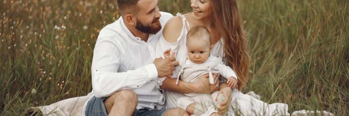 A joyful couple with their baby sitting on a blanket in a sunny meadow, embracing the beauty of summer.